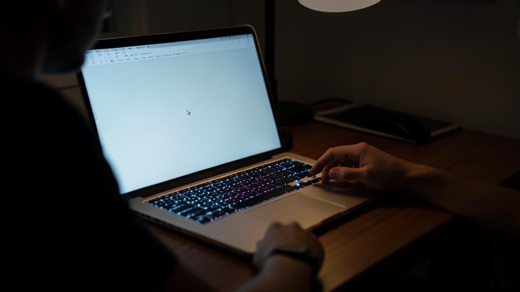 Une personne utilise un ordinateur portable avec un clavier rétroéclairé dans une pièce sombre.