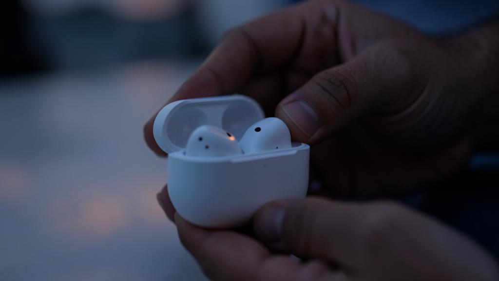 Unas manos sostienen una caja de carga abierta con dos auriculares inalámbricos, uno encendido.