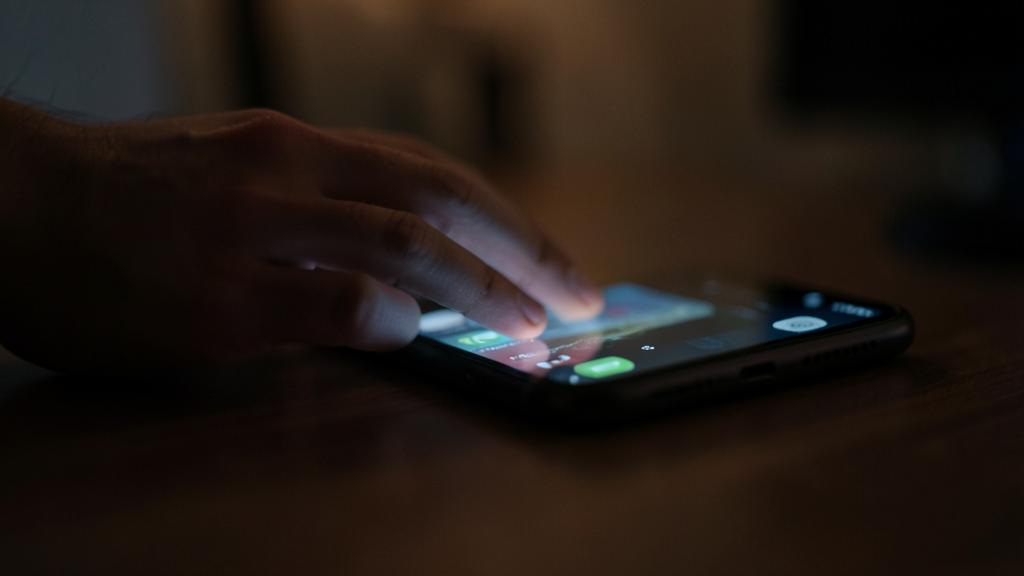 Una mano toca la parte trasera de un iPhone sobre una superficie, pantalla encendida.